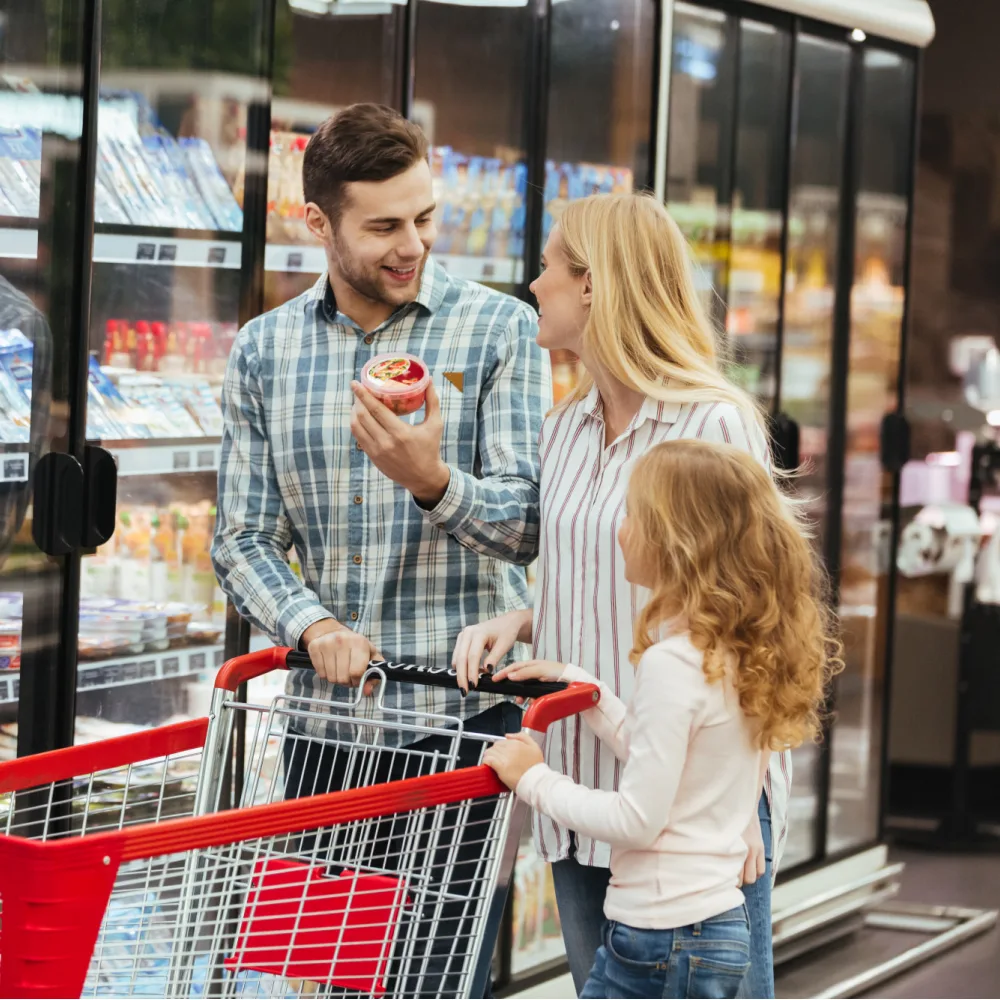 Rodzina z wózkiem sklepowym wybiera produkty przy chłodniach w supermarkecie